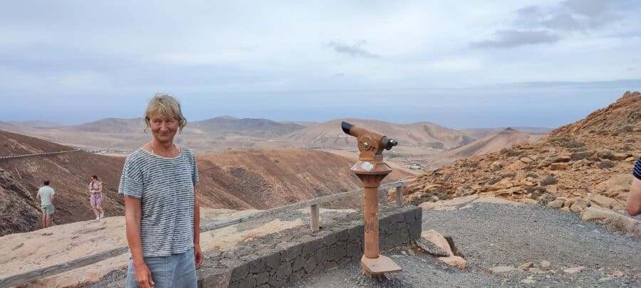 Pavlina steht auf einem Berg in der Wüste und schaut mit einem Fernrohr in die Weite.